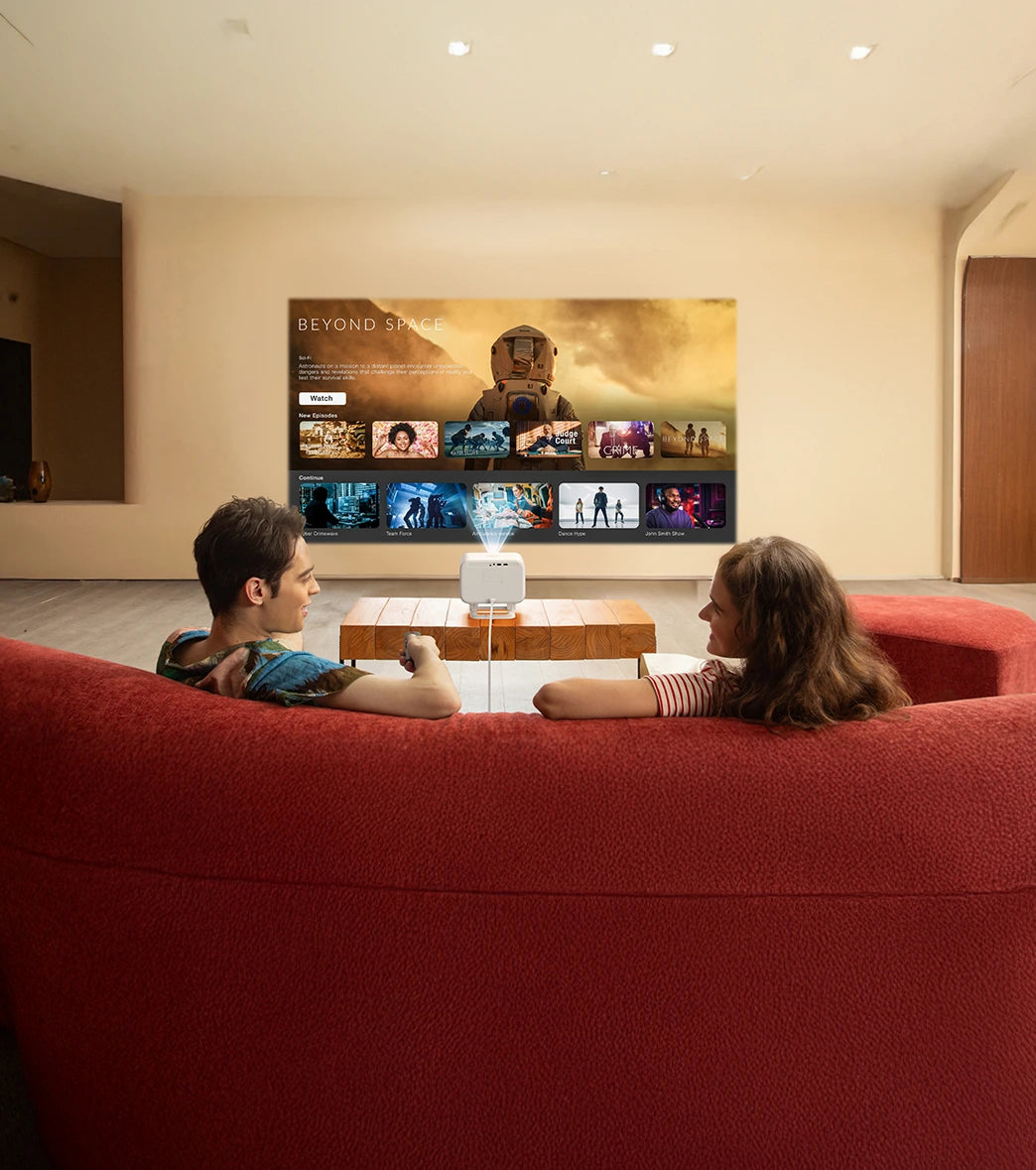 Two people sitting on a red couch watching on a yaber projector screen.
