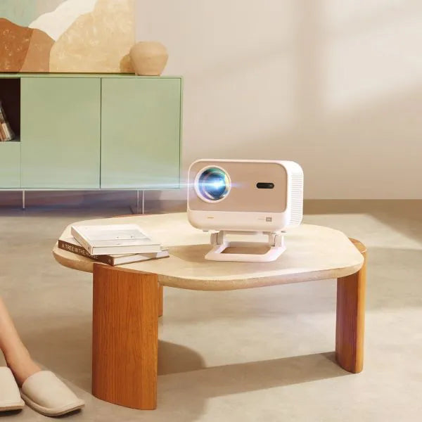 White Yaber projector on a wooden table with a screen projection in a room setting.
